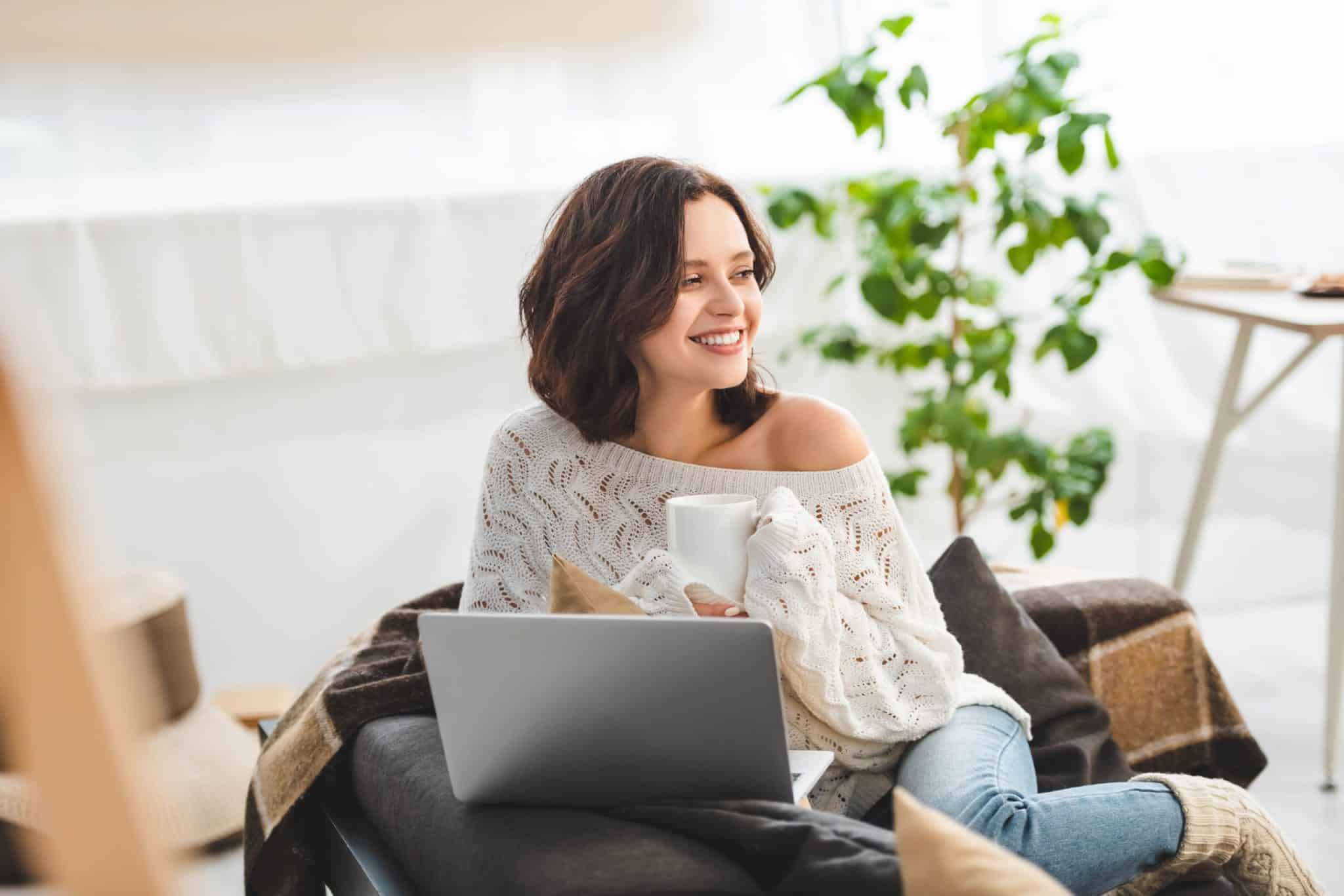 beautiful happy woman with cup of tea using laptop at cozy home