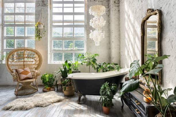 Comfortable bathroom with interior design in boho chic style, bathtub, vintage commode with mirror, wicker armchair, fluffy carpet and green houseplants in flowerpots