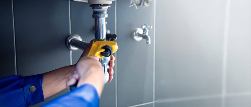 Plumber fixing white sink pipe with adjustable wrench.