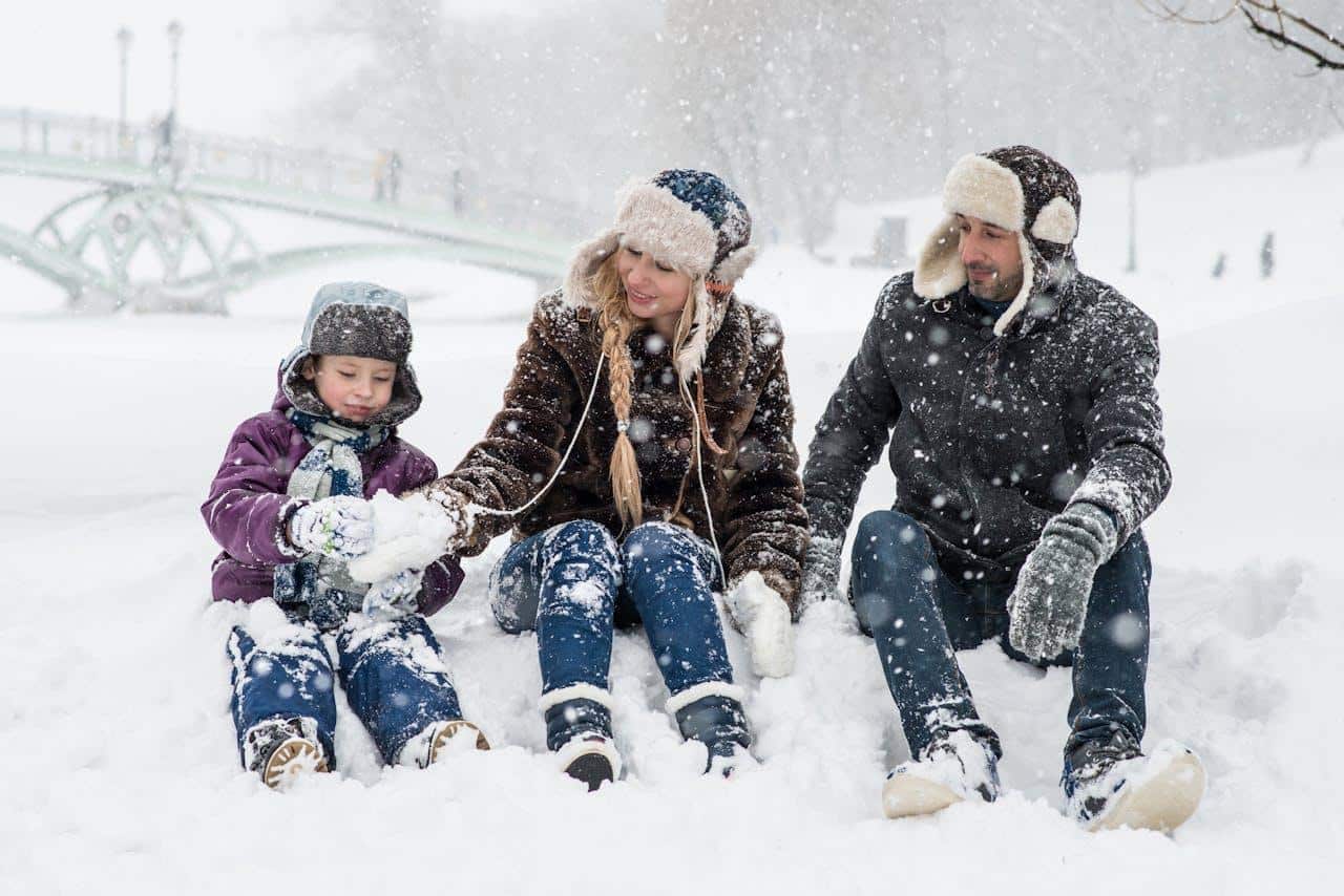 A photo of parents looking at their son while sitting on snow.