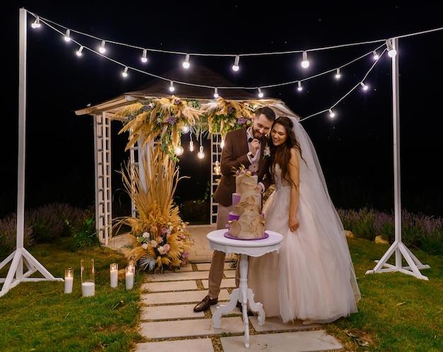 Outdoors evening ceremony of bride with traditional wedding cake